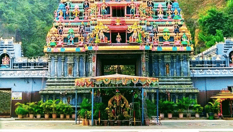 A vibrant facade of the Kanaka Durga Temple in Vijayawada featuring a multi-tiered temple gopuram against a green and hilly backdrop.