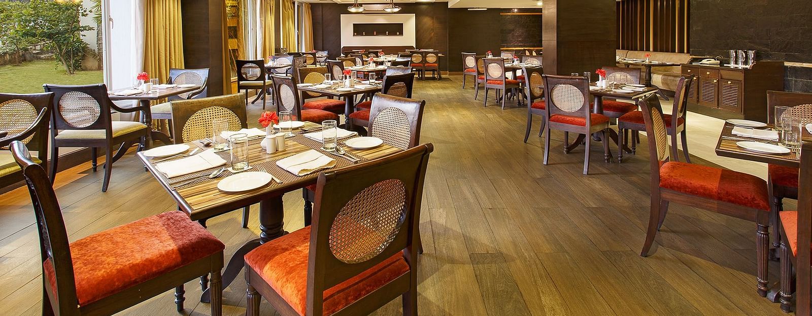A spacious restaurant with a wooden floor and exposed wooden beams on the ceiling. Large windows offer views of the outdoors.