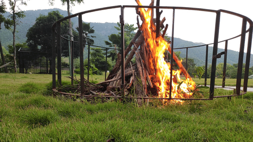 A large bonfire set up in a grassy area surrounded by protective fencing, ready for an evening gathering - Black Thunder, Coimbatore