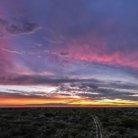 Vibrant sunset over a flat landscape with a dirt track.