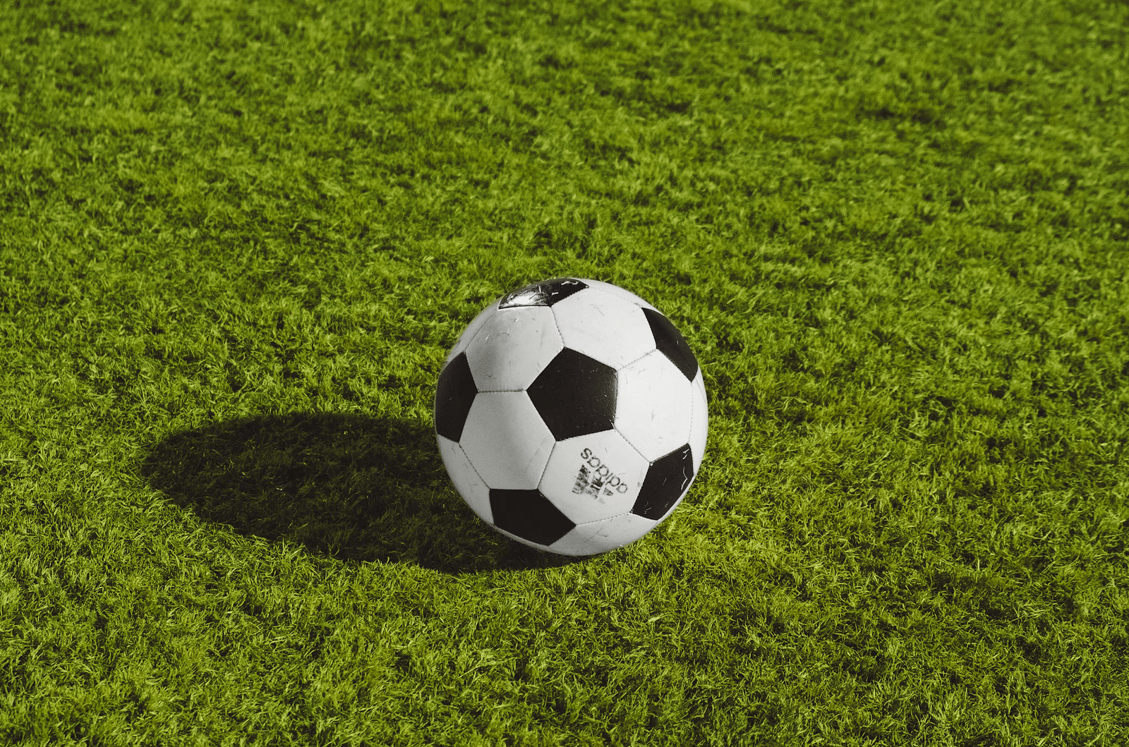 A soccer ball sits on bright green artificial turf, casting a slight shadow.