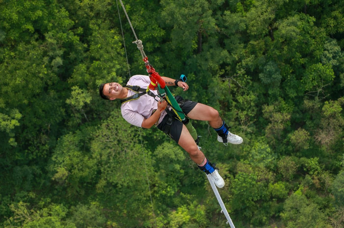 A person bungee jumping against a backdrop of dense forest.
