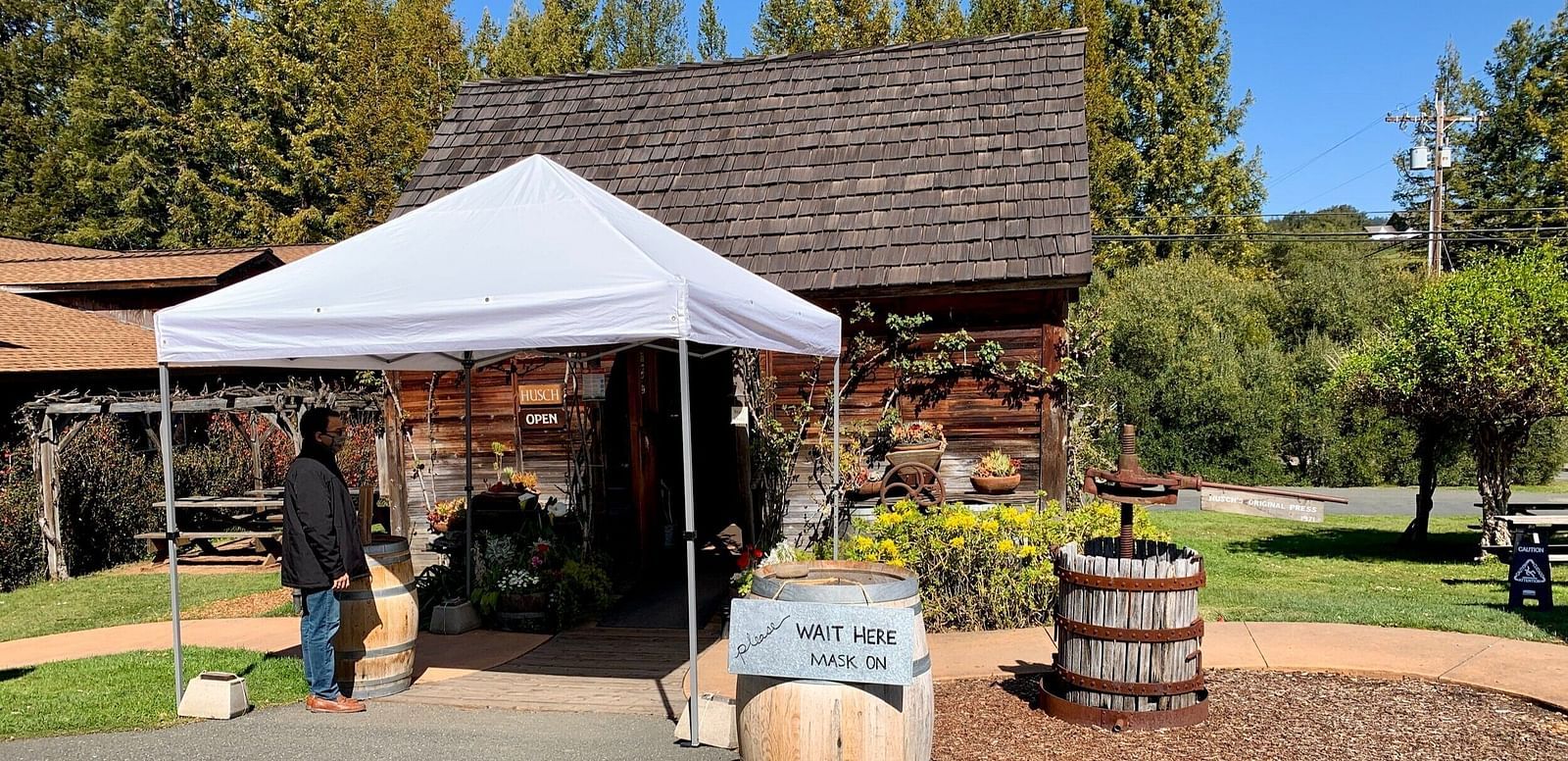 An image of an entrance of a vineyard which is made of wood and the area is surrounded by trees