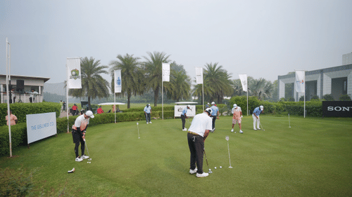 Golfers practicing putting on the green during an outdoor session at Karma Lakelands surrounded by palm trees and clubhouse views