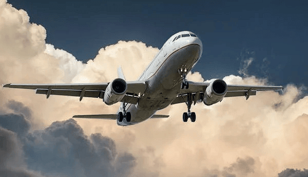 An airplane soaring through the sky with clouds in the background.