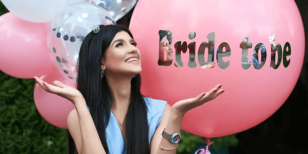 Happy bride-to-be with pink balloon and sash, celebrating her bridal shower with excitement and joy.
