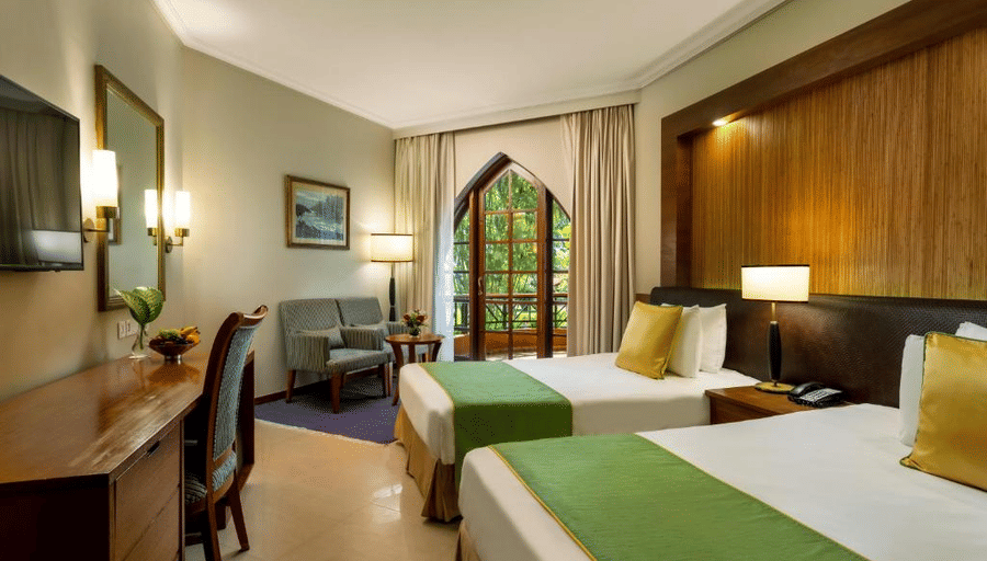 twin bed with golden pillow and green runner on it inside one of the rooms - Caravela Beach Resort Goa