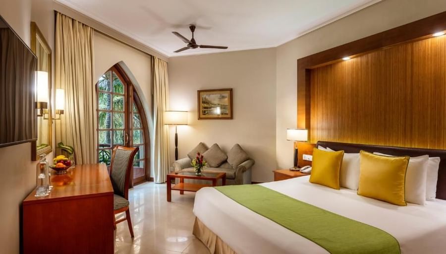 a double bed with golden pillow and green runner on it inside one of the rooms - Caravela Beach Resort Goa