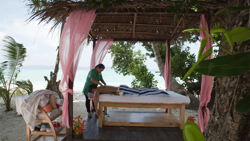 A masseuse massaging a client under a canopy by the beach in spa at Havelock.