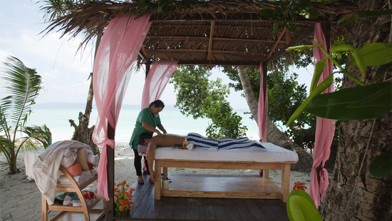 A masseuse massaging a client under a canopy by the beach in spa at Havelock.