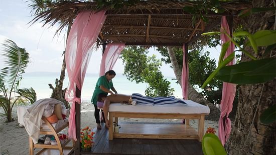 A masseuse massaging a client under a canopy 