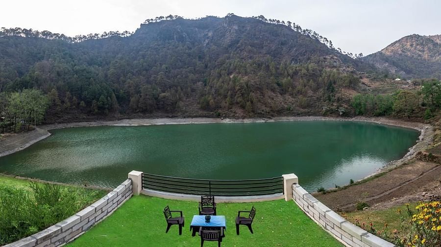 Open lawn with a table and chairs facing a serene green lake and forested hills.
