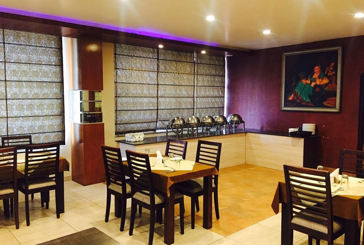 A dining room with a serene ambience, featuring a mix of wooden chairs and tables and a decorative screen - TGI Apple Inn, Jaipur 