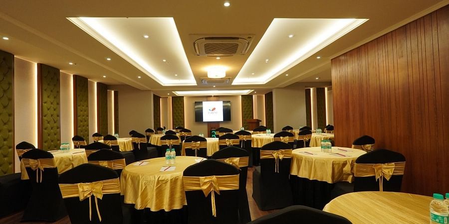 Well-lit conference room with a white projection screen, overhead projector, multiple rows of cushioned black chairs, and a grey carpeted floor – Magnus Nexstar Suites, Kalyani Nagar