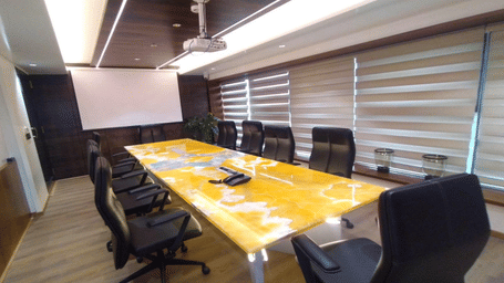 A wide angle shot of the Boardroom at the SRS Suites, Koramangala, featuring a yellow conference table in the middle surrounded by office chairs.