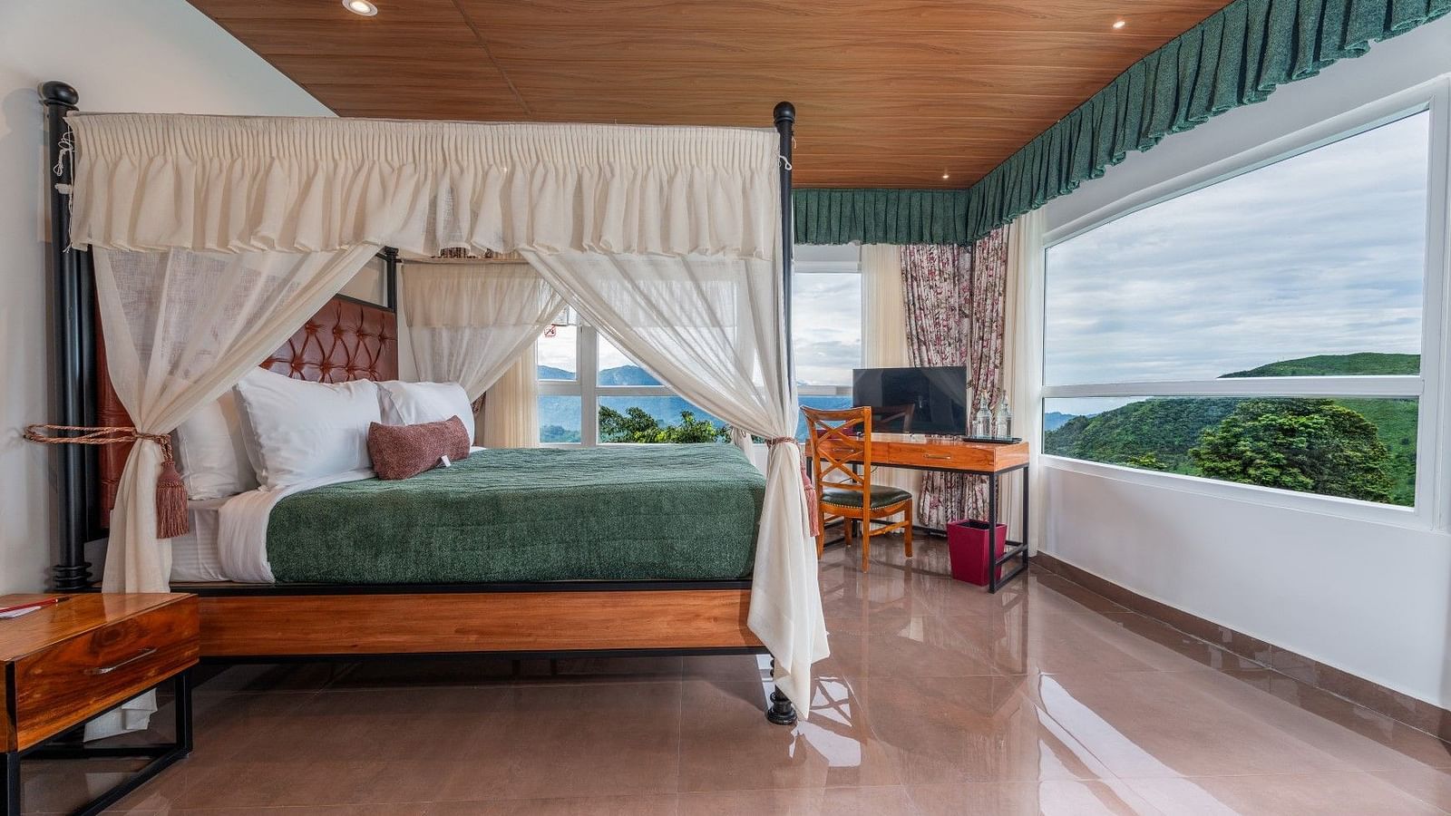  A generously sized bed with curtains on the sides, accompanied by wooden furniture and a breathtaking mountain view through the large windows.