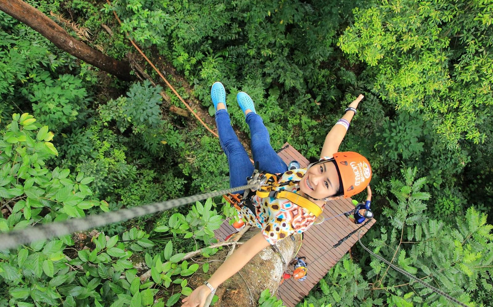 An image of a girl hanging from a cable with a backdrop of forest at the bottom