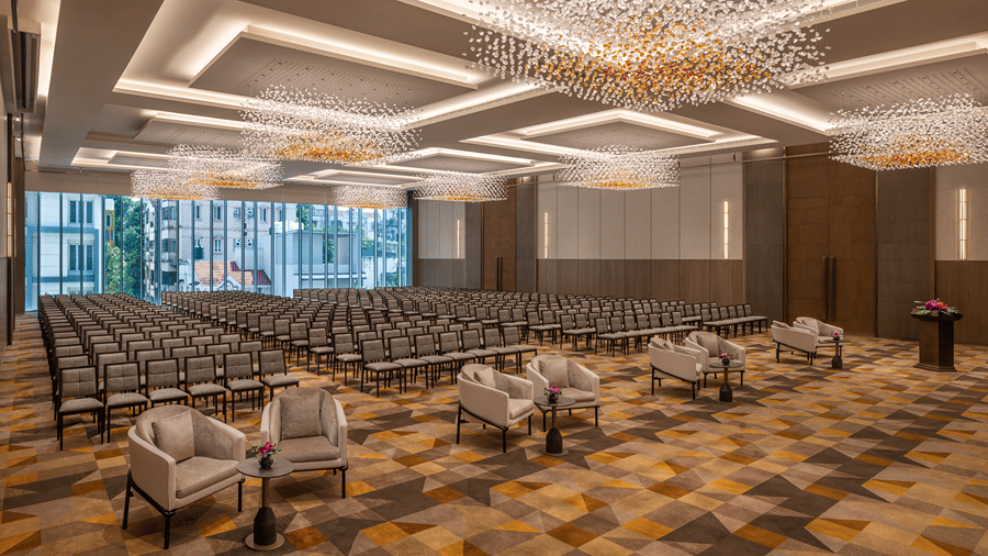 The grand banquet hall of Ballroom 1 arranged in theatre seating with plush armchairs in the front row and crystal chandeliers above at The Residency Towers Chennai.