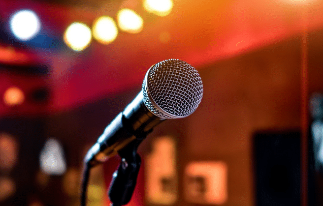 Microphone on stand, stage lighting in background, blurred colourful lights.