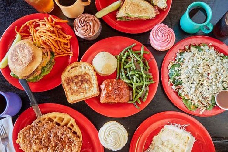 Top view of Spread of food like green vegetables, bread, burger, fries, waffles and other beverages placed on red plates and cups 