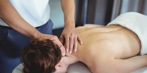 A pair of hands massaging the back of a person's neck lying face down on a massage bed