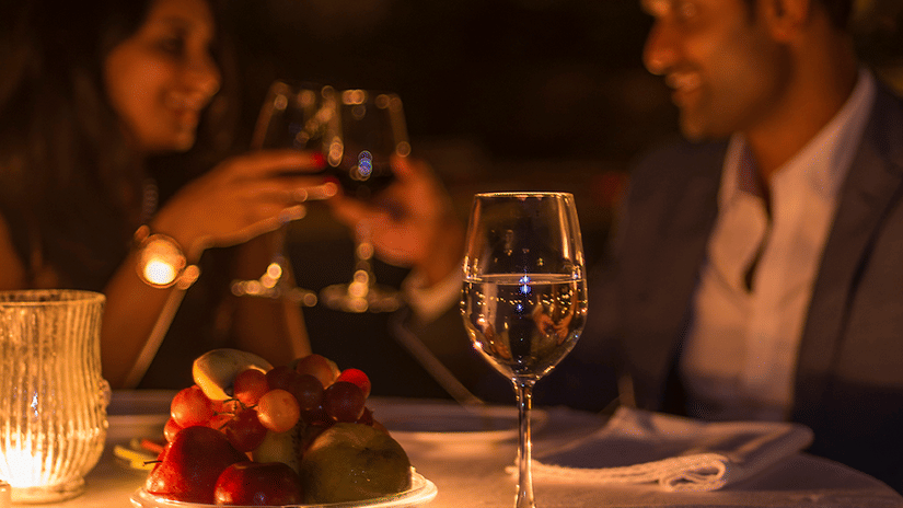 a couple toasting their wine glasses on their romantic candlelight dinner at The Serai, Chikmagalur. It is one of the many experiences in Chikmagalur that the resort provides for couples.
