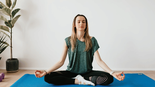 A woman sits cross-legged on a yoga mat in a peaceful indoor space, meditating with eyes closed and hands in mudra position at YO1 Longevity & Health Resorts.