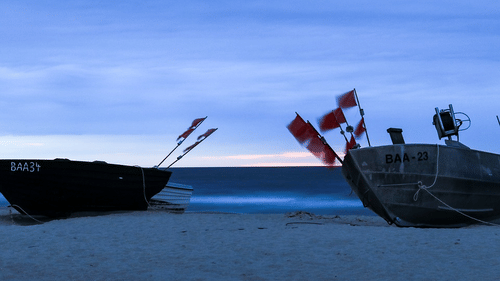 A pair of fishing boats anchored on the shore with flags hoisted against the sea and sky.