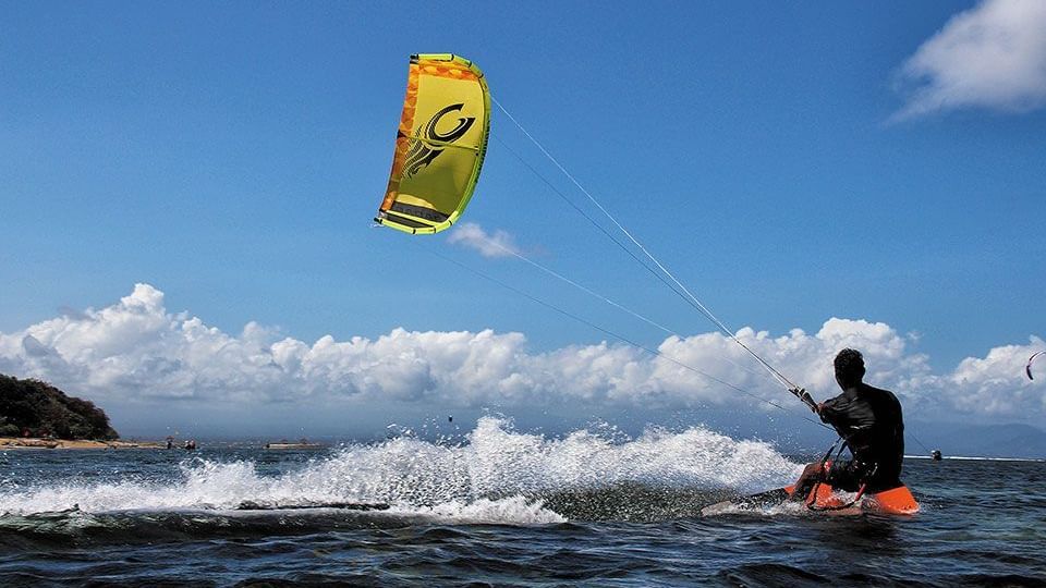 Person kite surfing on the vibrant blue waters of Antigua, with a bright yellow kite soaring against a sunny sky and ocean waves crashing below.