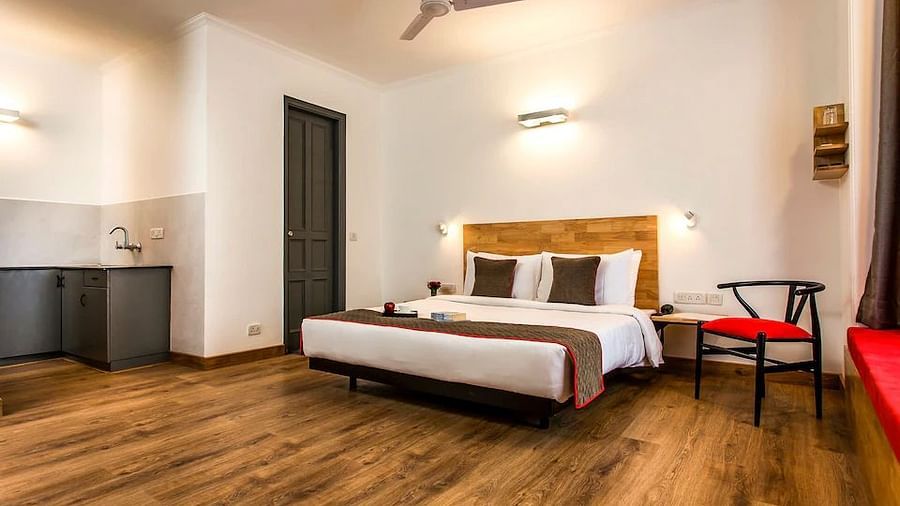 A spacious hotel room with a wooden bed, side chair and kitchenette with neutral tones - TGI Ameya Grand, Goa