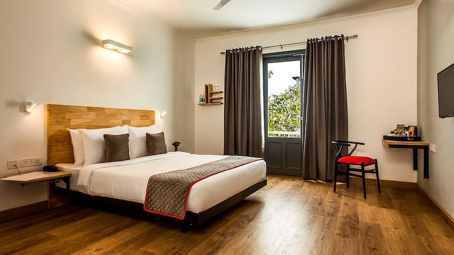 A modern hotel bedroom with a double bed, wooden headboard, gray curtains and a small desk with a red chair - TGI Ameya Grand, Goa