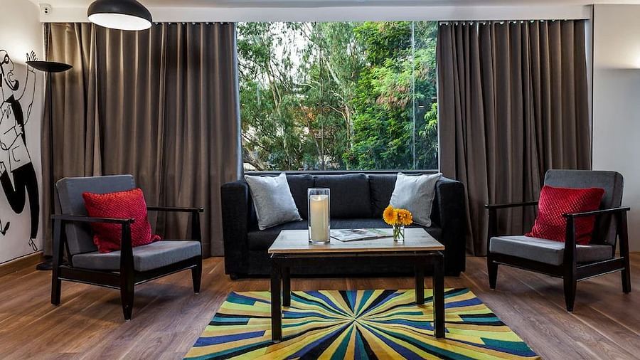 A chic hotel living room setup with two armchairs, a sofa and a vibrant rug, framed by heavy drapes and a wall art piece - TGI Ameya Grand, Goa