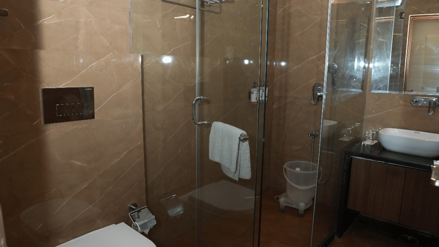 A bathroom featuring a clear glass shower enclosure, wall-mounted toilet, and sink counter at Bamboo Saa Sunrise Wedding & Wellness Resort, Jaipur.