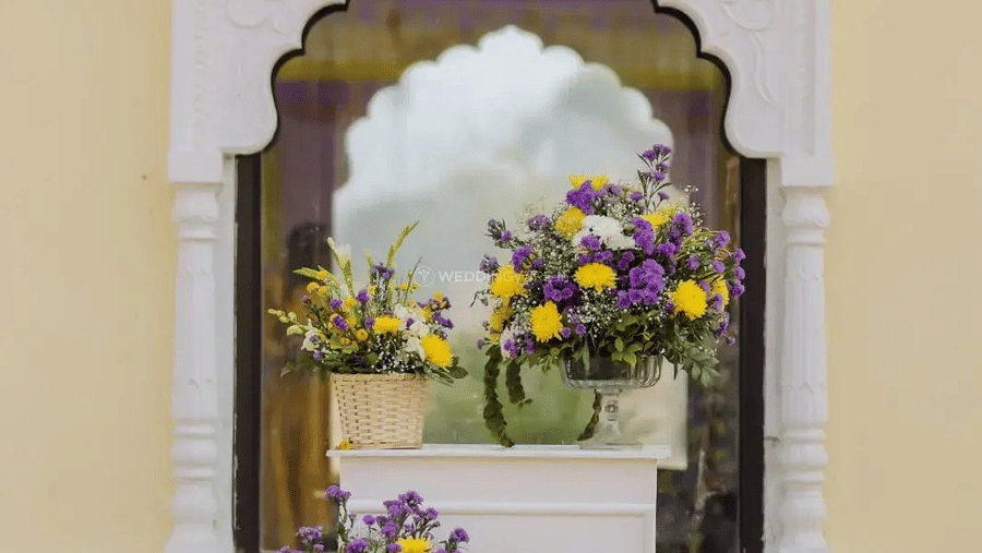 A floral arrangement placed in front of an arched mirror on a yellow wall with decorative framing at Beelwa Palace, Jaipur