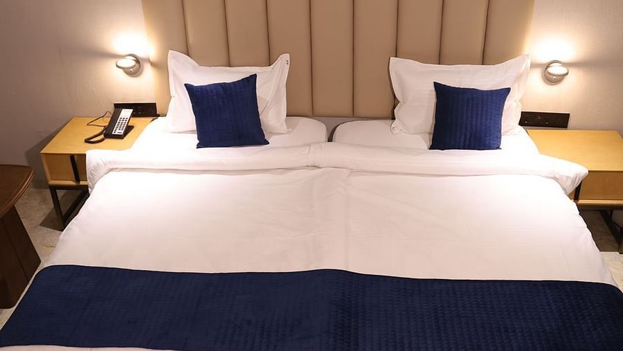 A comfortable twin bed setup at Lords Eco inn Jamnagar Maheshwari Nagar with crisp white and blue linens.