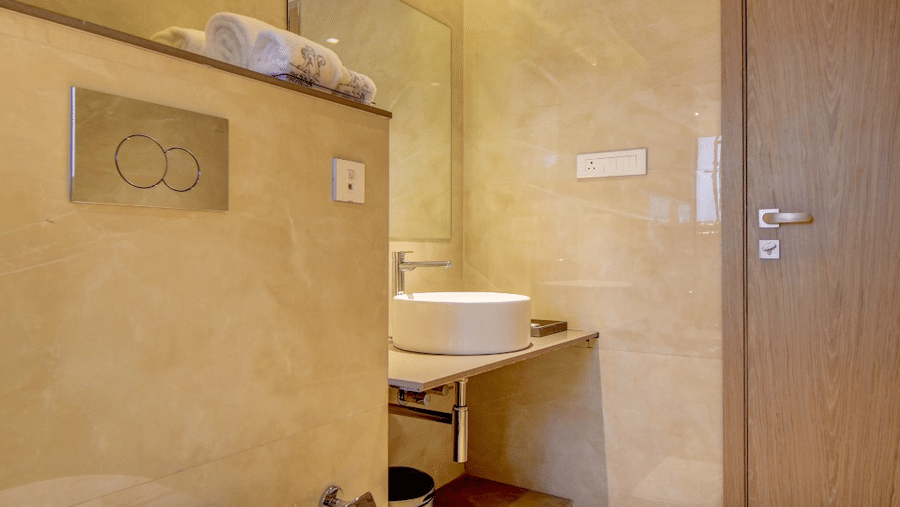 Bathroom of City View Suite at The SSK Solitaire Hotel and Banquets, Mumbai Naka featuring a commode, a sink and faucet , and towels placed on a shelve. 