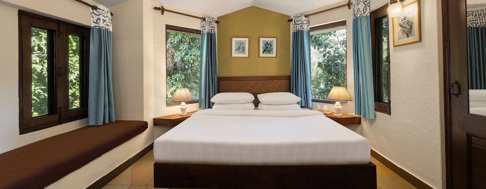 An image of a bedroom with double size bed, bedside table on either side, photos hanged on the wall and four windows from which natural lights are coming in - The Riverview Retreat,  Corbett