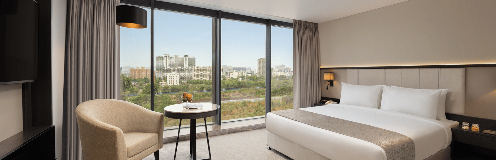  Premier Room with a king size bed and a sofa beside a large window at Essentia Premiere, Pune.