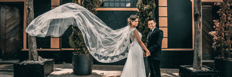 Wedding pose by a married couple in a typical Christian wedding attire with a large vase of pines and a structured emerald coloured house at the background.