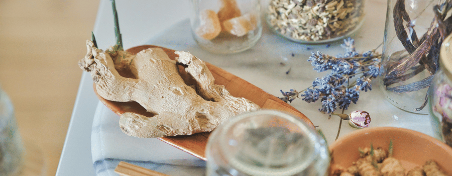 A selection of jars and bowls containing dried herbs, spices, and roots arranged for a wellness treatment.