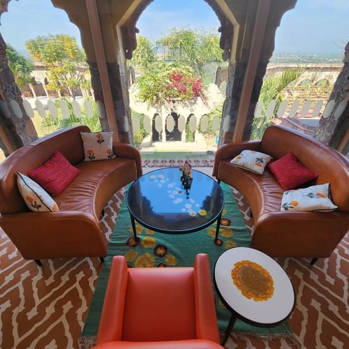 Two curved sofas face each other with a table between them, viewed through arched openings at Tijara Fort-Palace - 19th Century, Alwar.