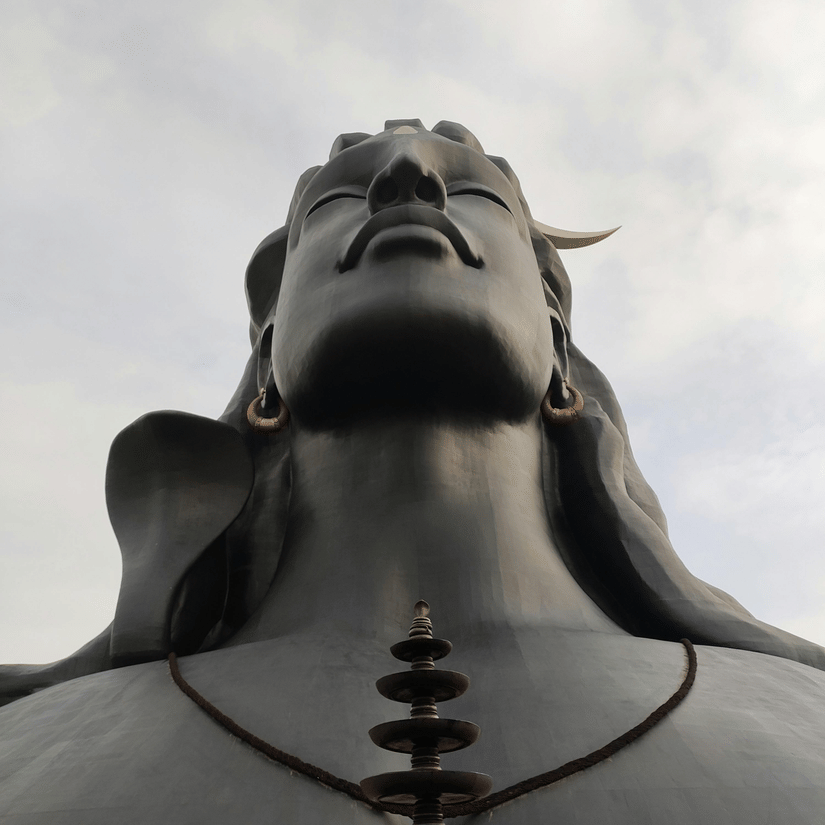 Dark statue of a hindu god with his eyes closed looking up at the sky under a cloudy sky