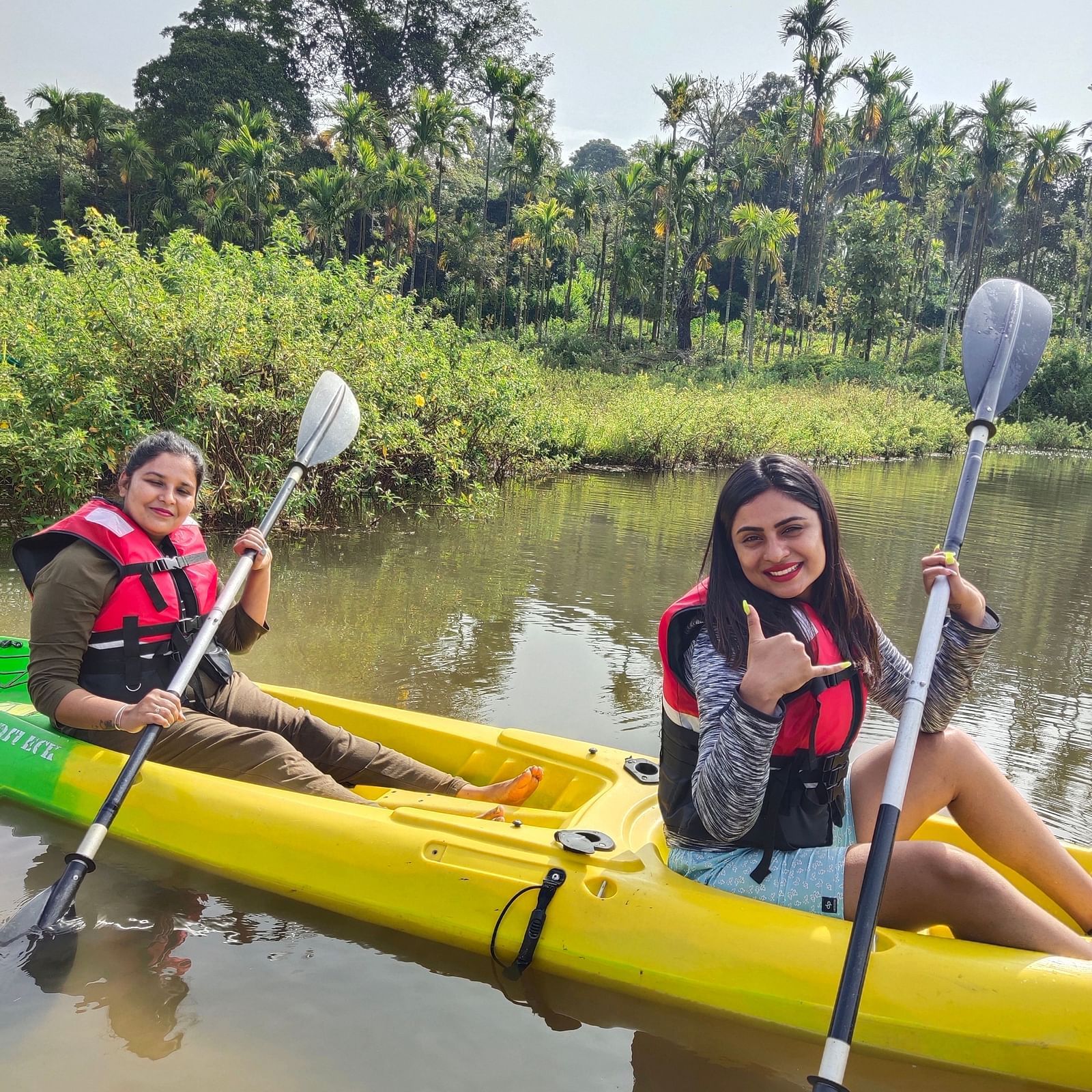 Two women in life jackets smiling while kayaking on a serene river with dense foliage in the background - Evergreen County