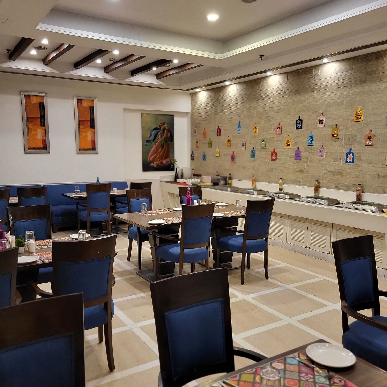 An image of a restaurant featuring multiple sets of chairs and tables where plates, cutlery and napkins are placed at Inde Hotel Signature Tower Gurgaon
