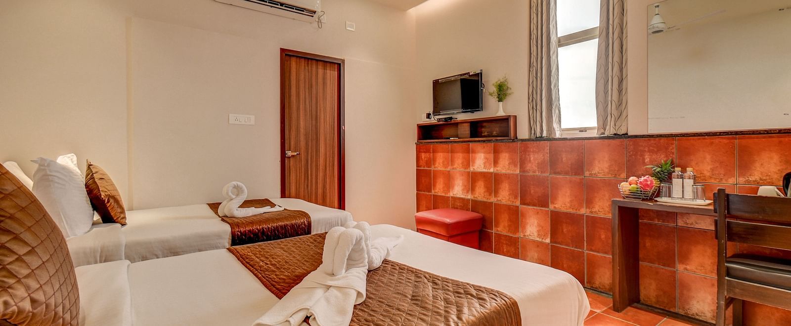 A spacious room at Harigovinda's JNStay with two beds, a wall-mounted TV, and a wooden desk to the side
