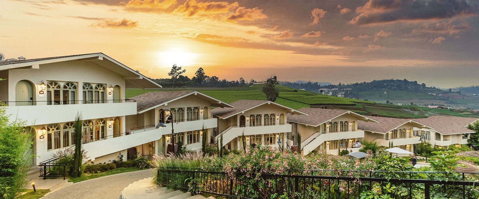 Walkway weaving through Mango Hill Shola, Ooty, flanked by resort buildings and landscaped surroundings.