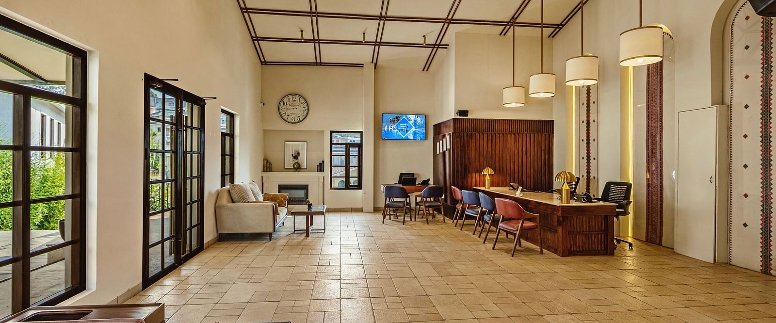 Bright interior hallway at Mango Hill Shola, Ooty, with tiled floors, wide windows allowing natural light, and casual seating arrangements along the corridor.
