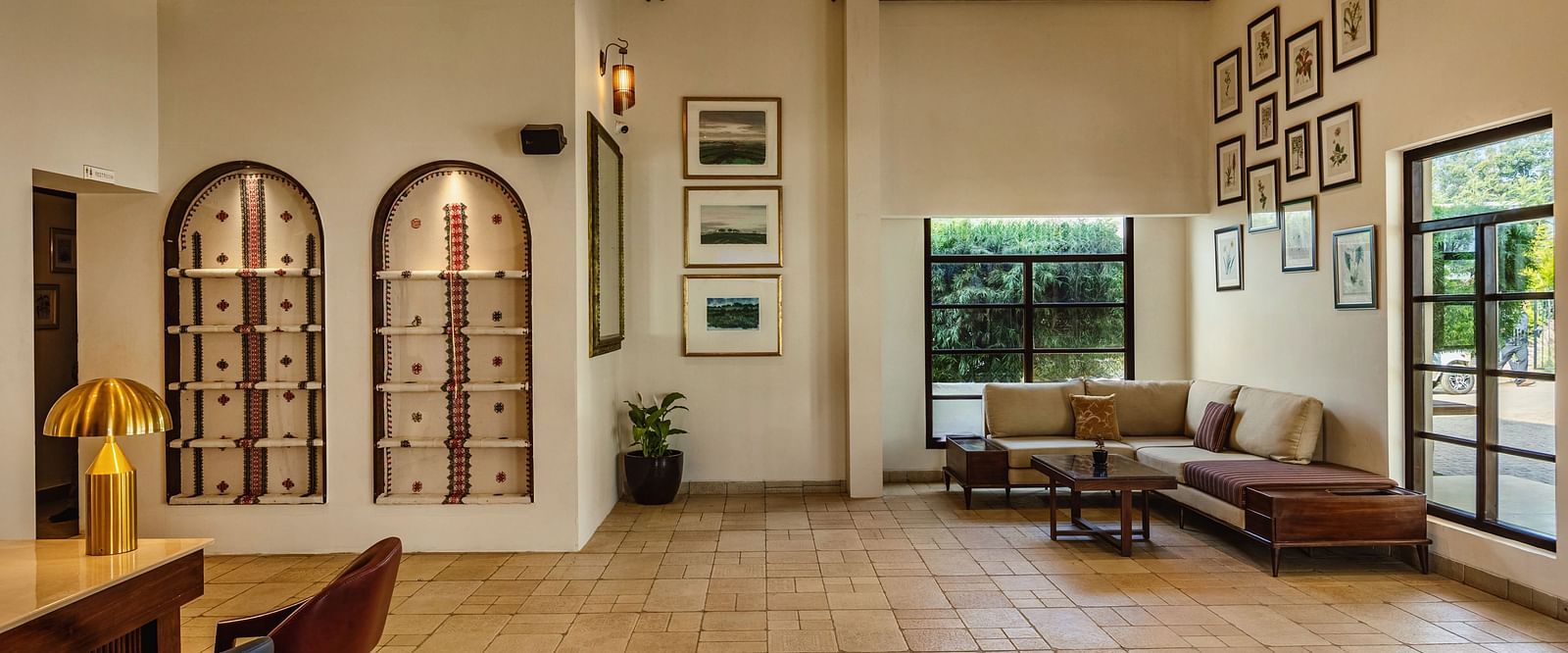 A side angle view of a welcoming indoor area at Mango Hill Shola, Ooty, with tiled flooring, cushioned seating, and expansive windows offering plenty of daylight.