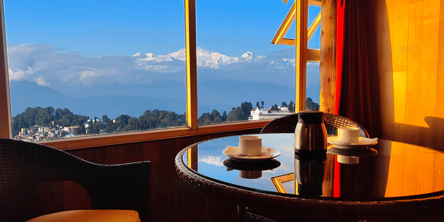 Panoramic window view with seating area and hillside scenery at Mount Thistle Boutique Hotel, Darjeeling.