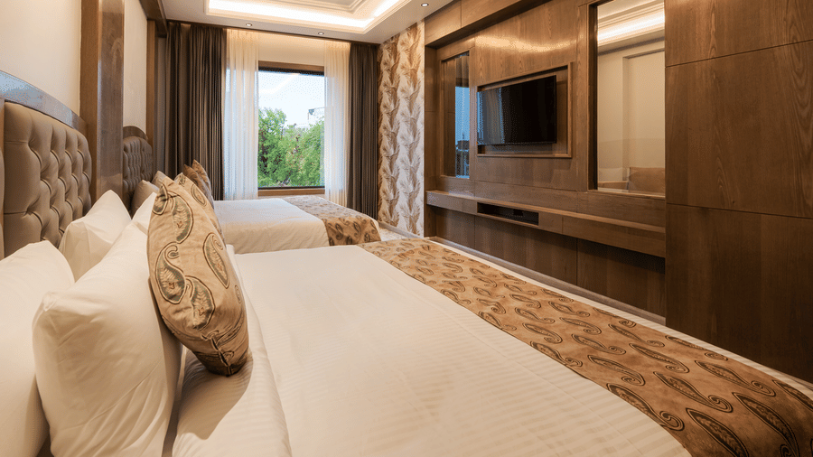 A spacious guest room with two single beds, dark wood wall panelling, and a large window at Ananta Express, Katra.